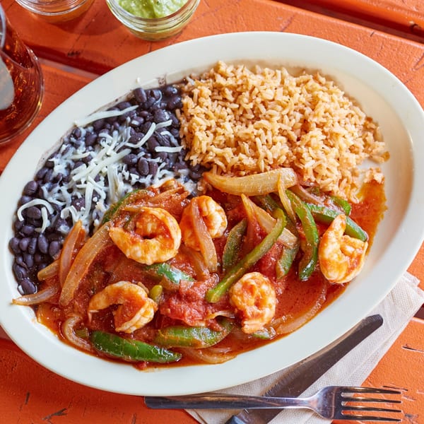 El Sancho Loco's shrimp fajitas with rice and black beans, served on a white oval plate.