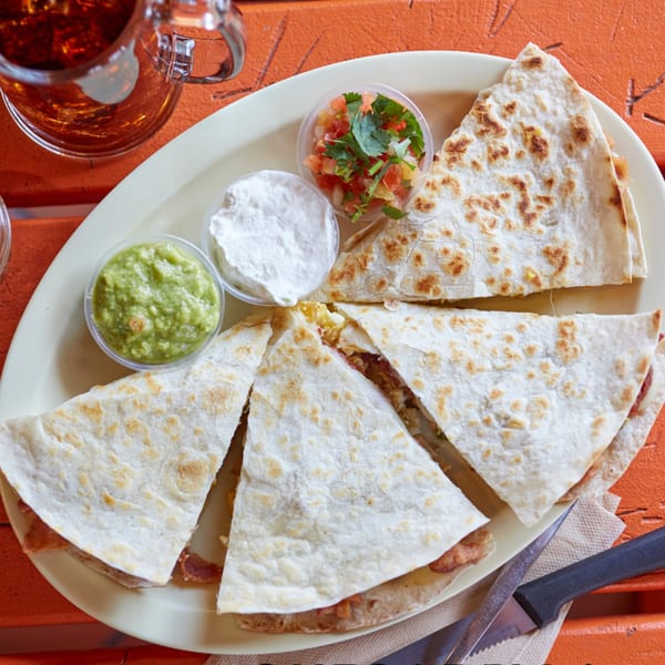 El Sancho Loco quesadillas with guacamole, sour cream, and salsa on an orange table.