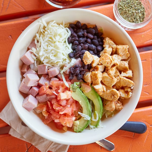 A colorful Mexican salad bowl with chicken, ham, black beans, cheese, tomatoes, and avocado.