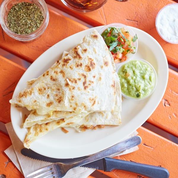 El Sancho Loco's cheese quesadillas with sides of guacamole and pico de gallo on an orange table.